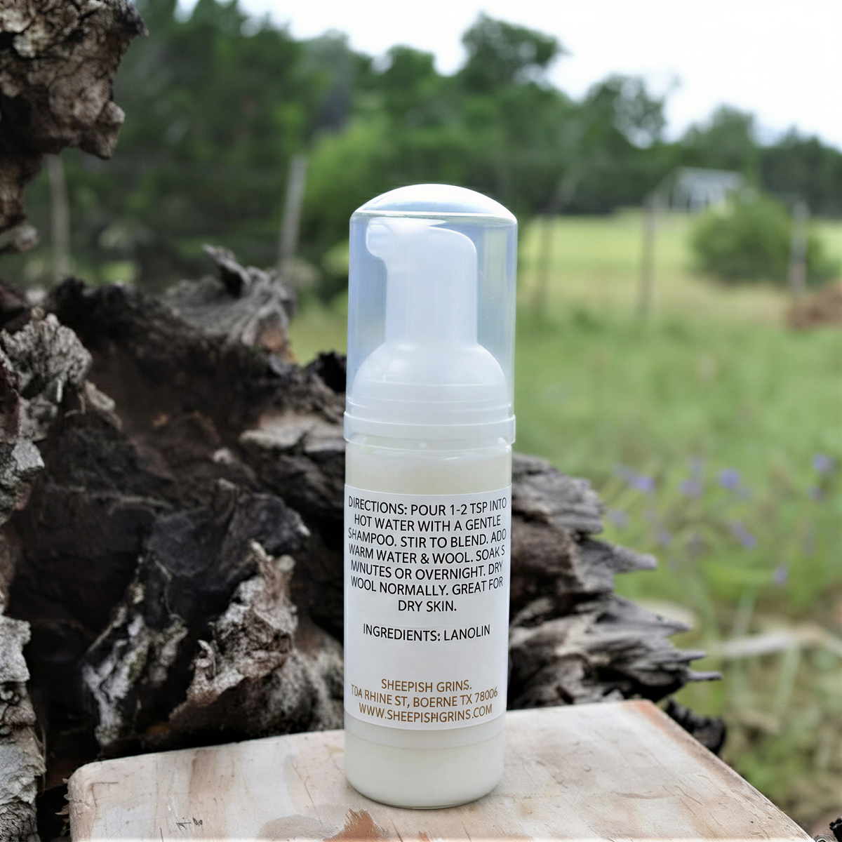 A bottle of Llanil body wash is placed on a wooden surface, with a natural background of trees and grass.