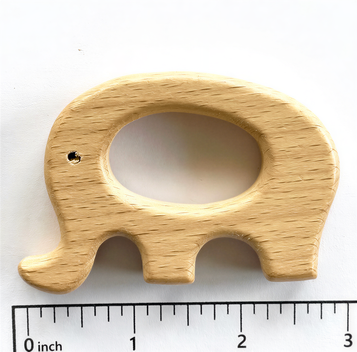 A wooden elephant-shaped teething toy is placed next to a ruler for size comparison.