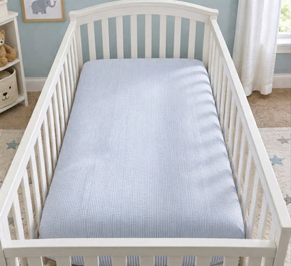 A white crib with a blue striped mattress in a nursery.