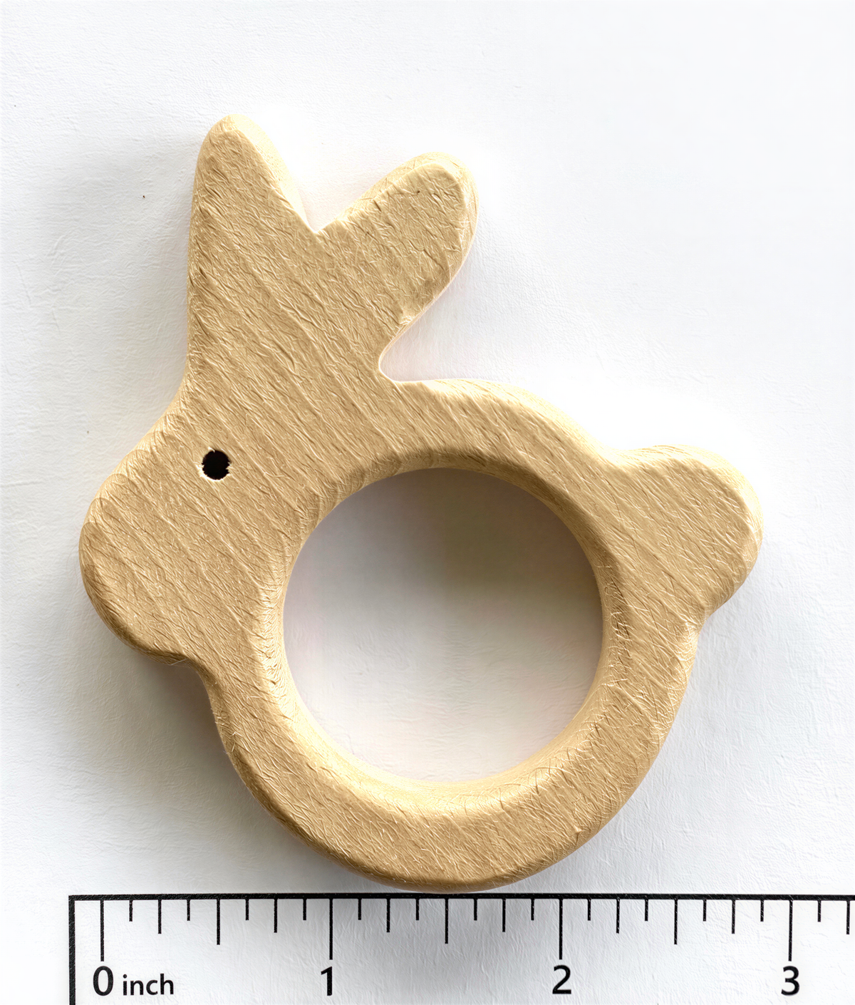 A wooden binky toy in the shape of a rabbit, with a hole in the center, is shown against a white background.
