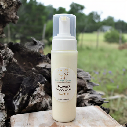 A bottle of "Sheep's Grown" Foaming Wool Wash, a natural and calming product, is displayed against a blurred background of a wooded area.