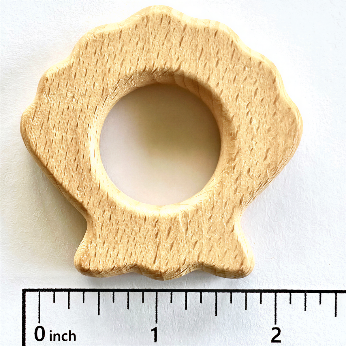 A wooden toothbrush holder in the shape of a seashell, with a scale ruler indicating its size.