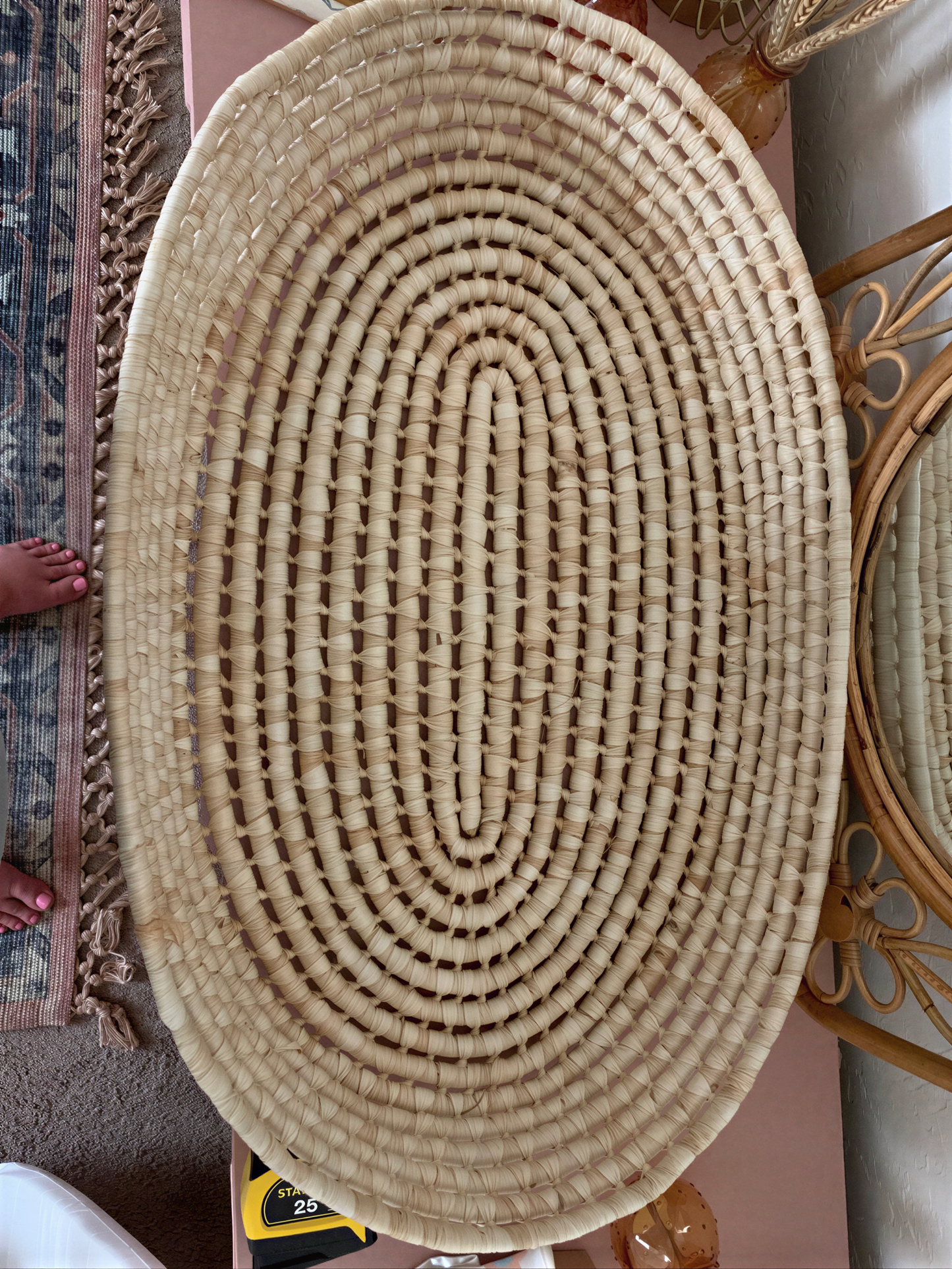 a woven basket with a circular pattern, placed on a pink surface.