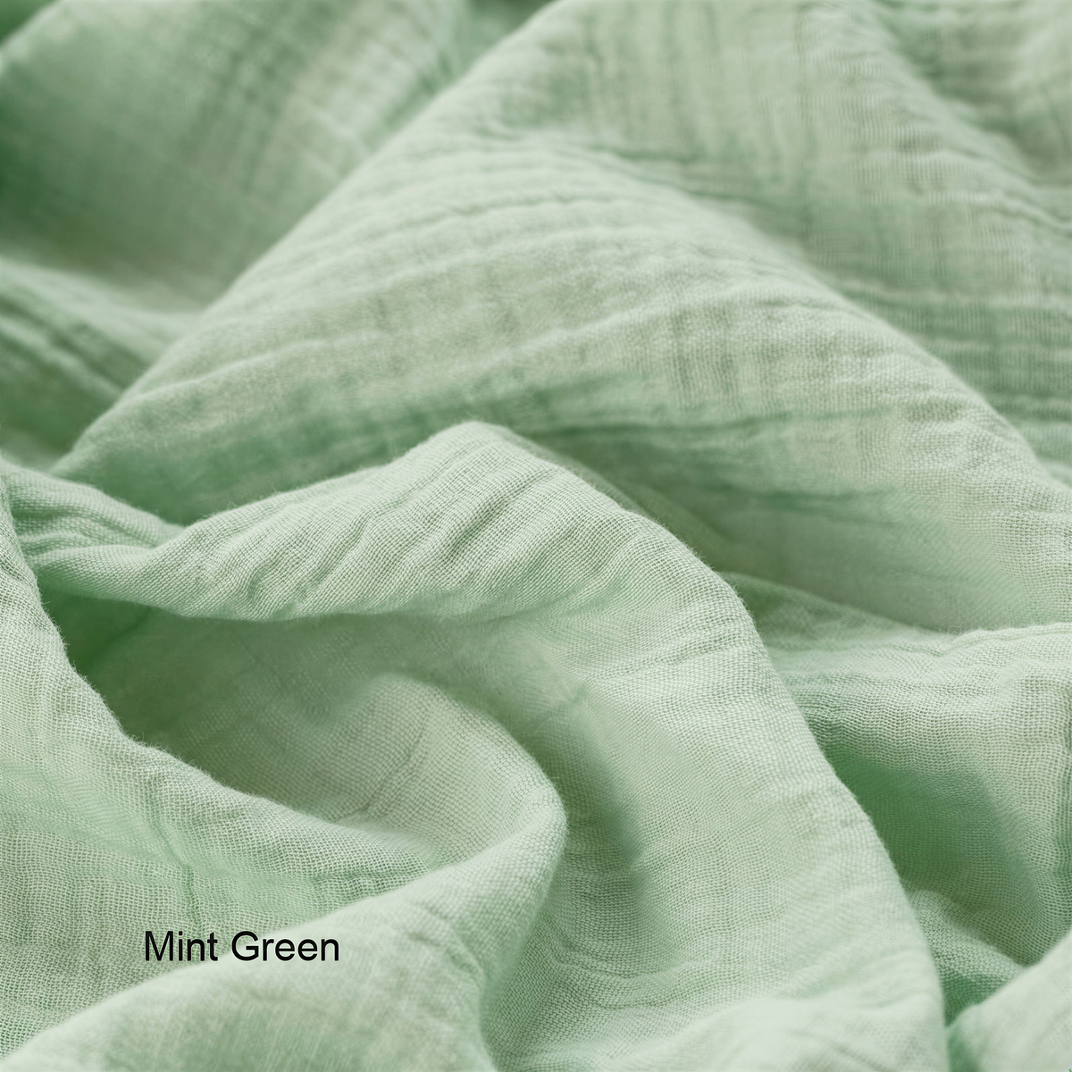 A close-up view of a soft, mint green fabric, possibly cotton or linen, with a slightly wrinkled texture.