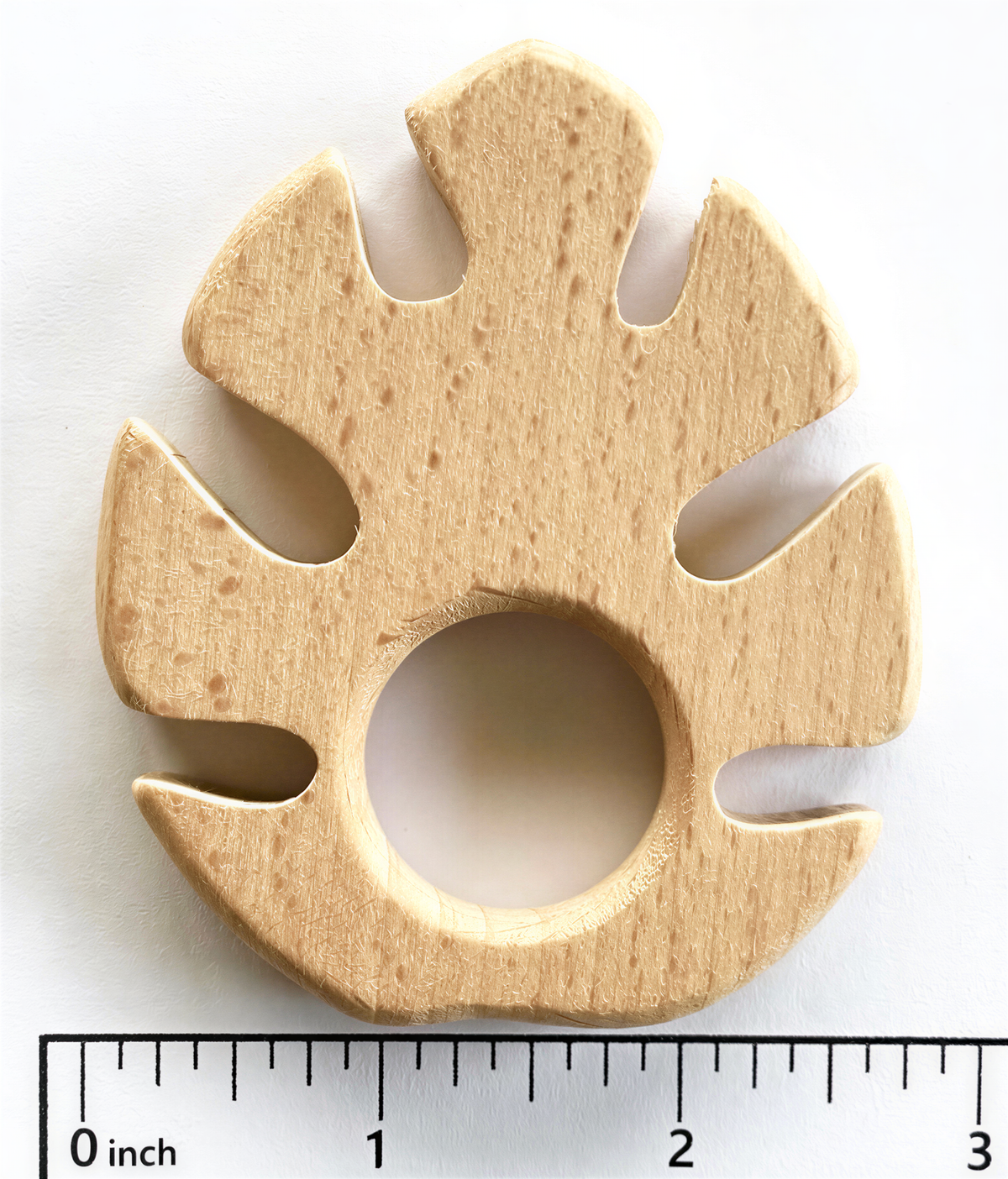 A wooden teething toy in the shape of a leaf, with a hole in the center, is shown against a white background.