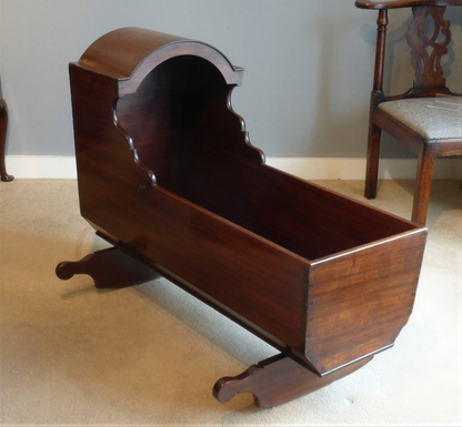A wooden rocking crib with a curved top and a curved seat is placed on a beige carpeted floor.