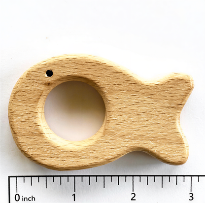 A wooden fish-shaped toothbrush holder with a hole in the center, placed next to a ruler for scale.