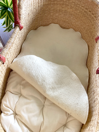 A woven basket containing a white cloth, possibly a blanket or a sheet, with a scalloped edge.