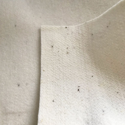 a close-up view of a white fabric with small black specks or specks of dirt on it.